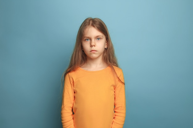 serious teen girl on a blue studio background. Facial expressions and people emotions concept.