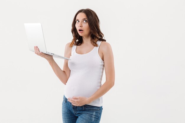 Serious thinking pregnant woman using laptop