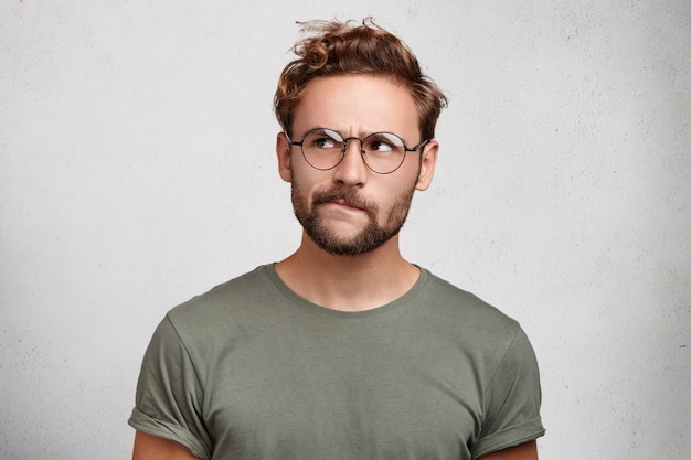 Free photo serious thoughtful clever scientific worker wears spectacles, has beard, curves lower lip,