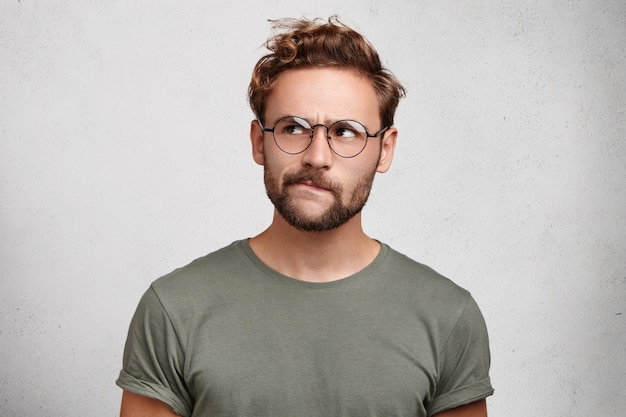 Serious thoughtful clever scientific worker wears spectacles, has beard, curves lower lip,