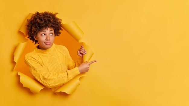 Serious thoughtful dark skinned millennial girl with afro bushy hair points away on copy space