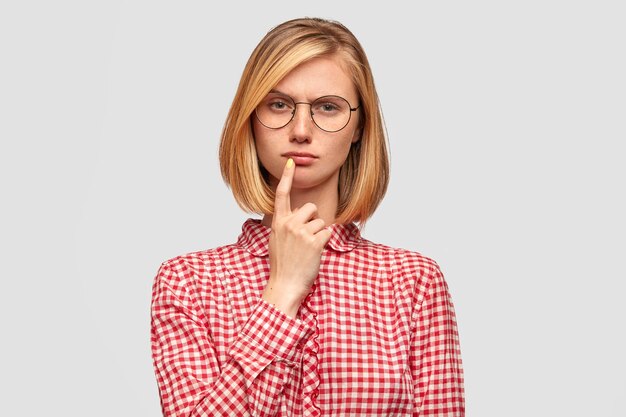Serious thoughtful woman student has clever expression, keeps fore finger near mouth