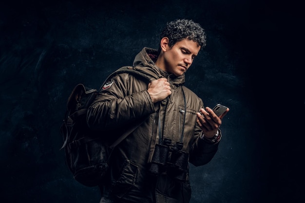 Serious traveler with binoculars looking into the phone pictured sideways on a black background