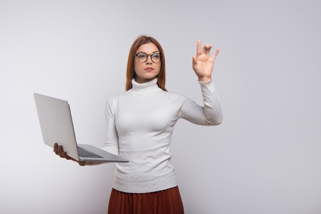 Serious woman holding laptop and touching air with hand