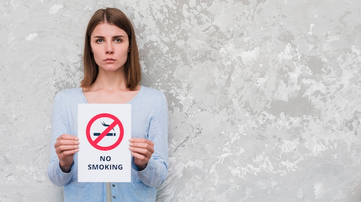 Free Photo serious woman holding with no smoking text and sign standing against weathered wall