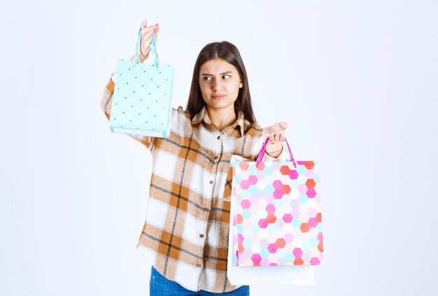  serious woman looking at bunch of shopping bags over white wall. 