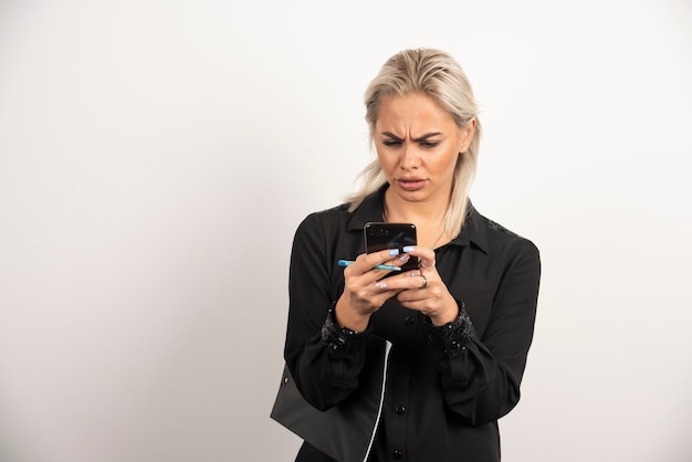 Serious woman looking on mobile phone and holding a clipboard . High quality photo