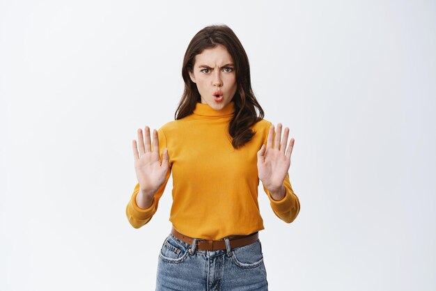 Serious woman say no showing stop gesture and frowning with disapproval disagree and forbid something bad standing against white background