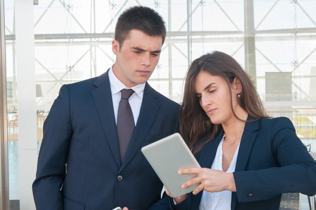 Serious woman showing concentrated man data on tablet