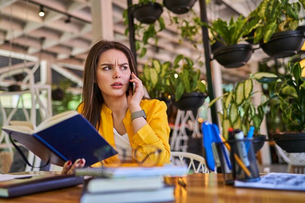 Serious woman speaking by mobile phone in office.