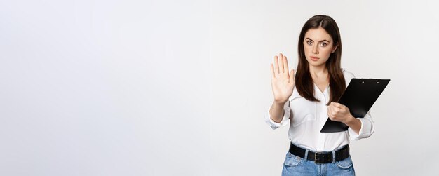 Free photo serious woman with clipboard documents extending arm showing taboo stop sign disapprove prohibit smt