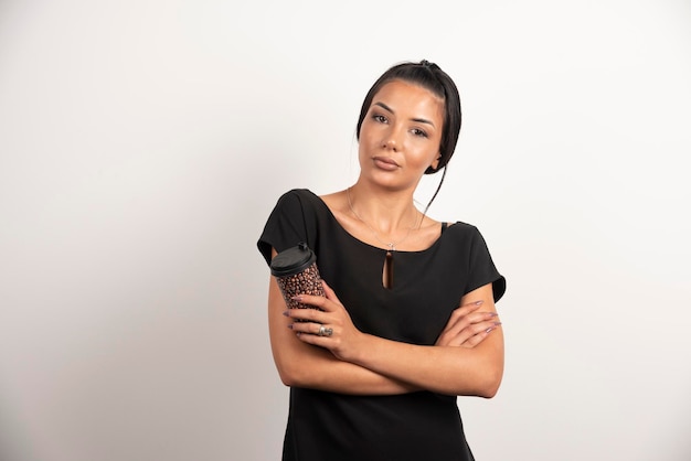 Serious woman with cup of coffee standing on white wall.