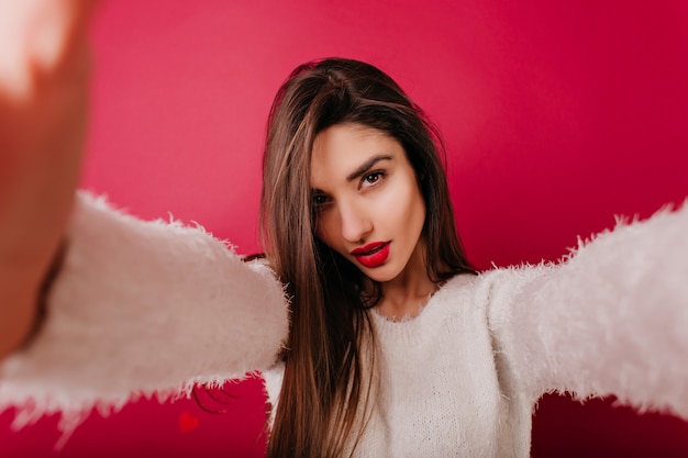 Serious woman with straight shiny hair taking picture of herself