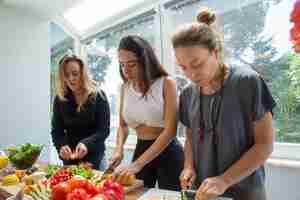 Foto gratuita donne seri che cucinano e che tagliano le verdure in cucina