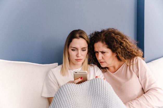 Serious women using smartphone on sofa