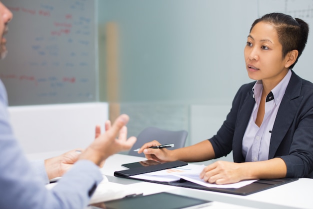 Serious young Asian executive listening to male employee