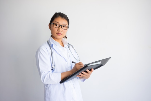 Serious young Asian female doctor writing medical prescription. 