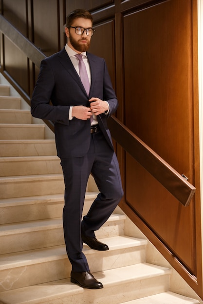 Serious young bearded businessman standing on ladder indoors