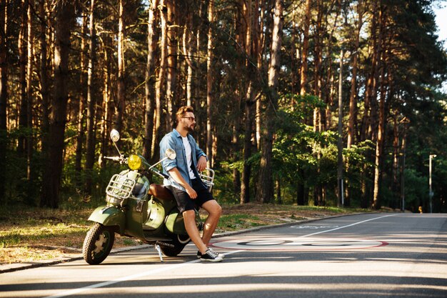 Serious young bearded man standing near scooter