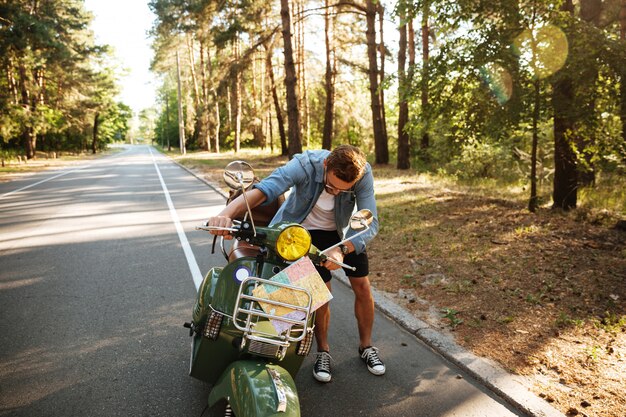 Serious young bearded man standing near scooter