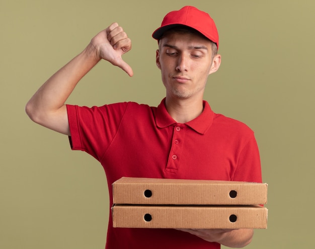 Серьезный молодой блондин доставщик недурно держит и смотрит на коробки для пиццы