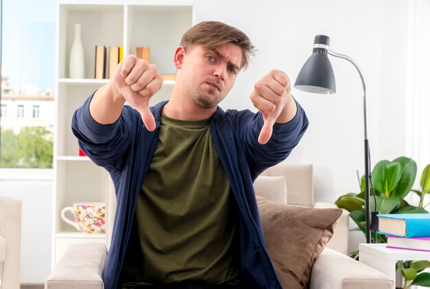 Serious young blonde handsome man sits on armchair