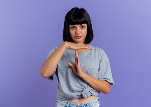 Serious young brunette caucasian girl gestures time out hand sign isolated on purple background with copy space