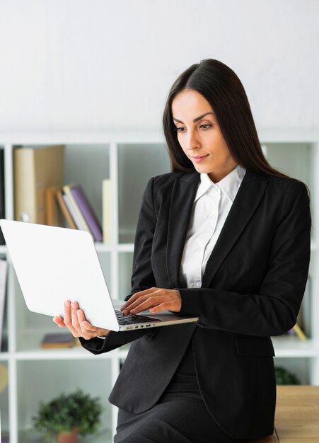 Serious young businesswoman looking at laptop hold in her hand
