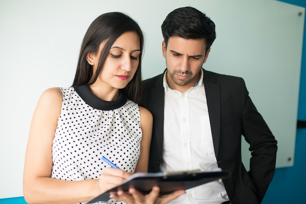 Serious young businesswoman showing documents to male executive