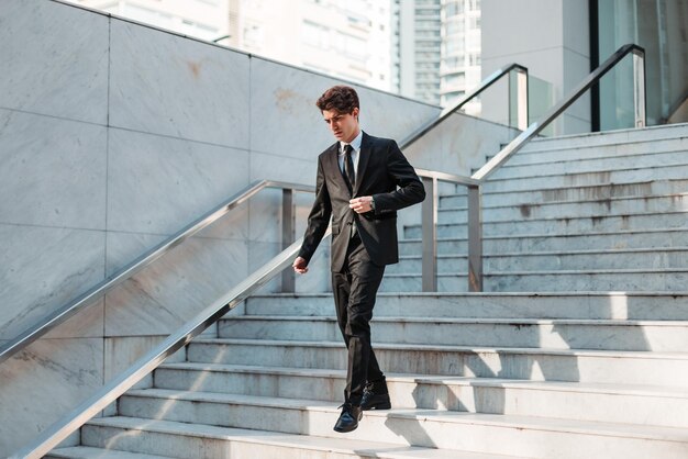 Serious young Caucasian guy dressed professionally walking down outdoor stairs