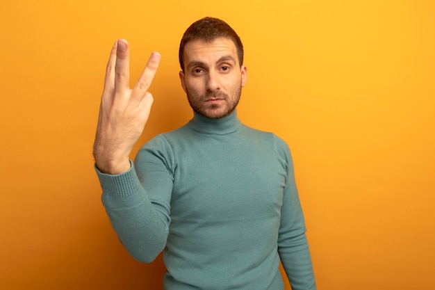 Free photo serious young caucasian man  showing three with hand isolated on orange wall with copy space