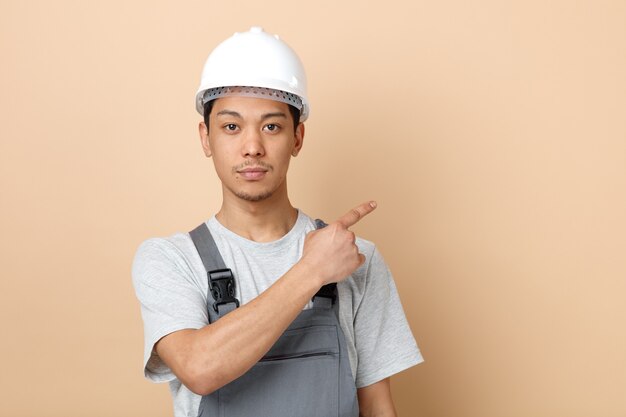 안전 헬멧과 측면을 가리키는 유니폼을 입고 심각한 젊은 건설 노동자