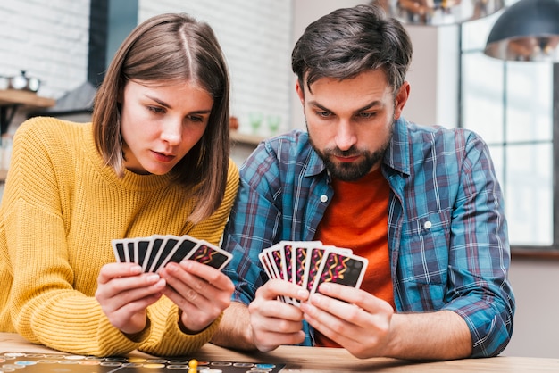 Серьезная молодая пара смотрит на свои карты, играя в настольную игру