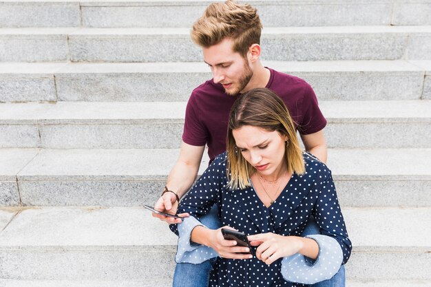 Serious young couple sitting on staircase looking at cellphone