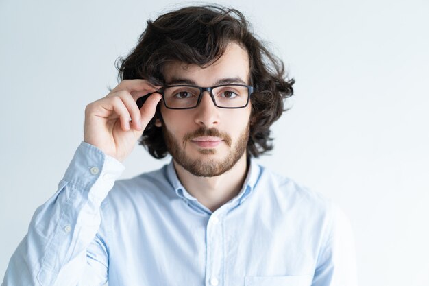 Free photo serious young dark-haired man adjusting glasses