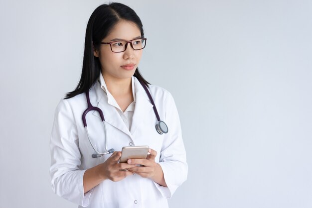 Serious young female doctor using smartphone