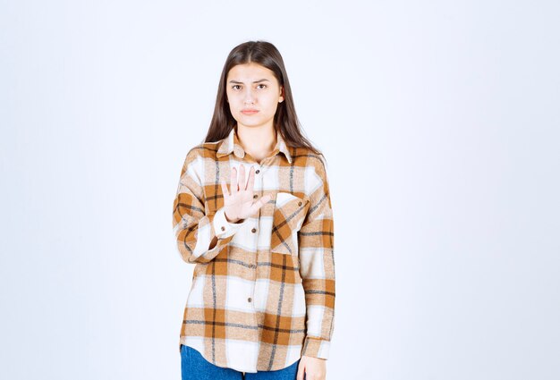 a serious young girl model standing and showing stop sign . 