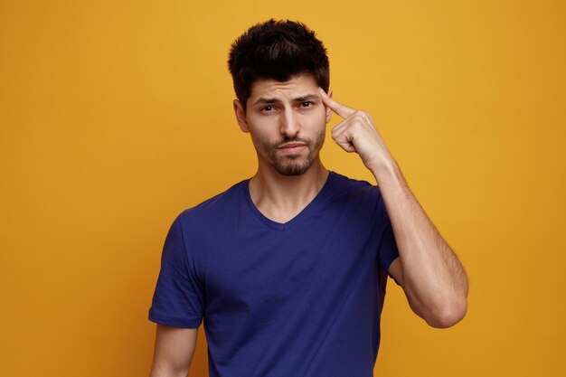 Serious young handsome man looking at camera doing think gesture on yellow background