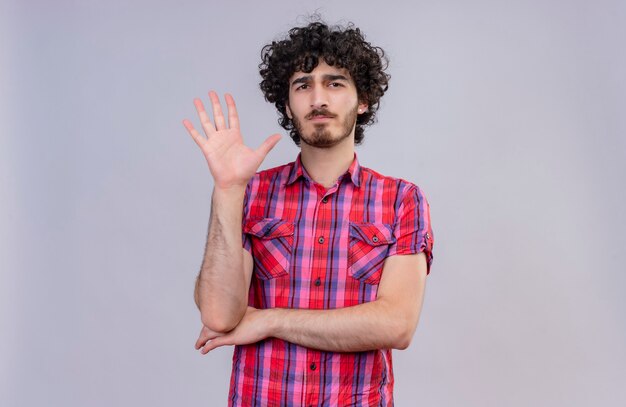 A serious young handsome man with curly hair in checked shirt showing five fingers raising hands 