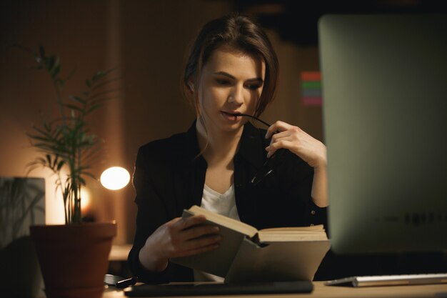 Serious young lady designer reading book. Looking aside.