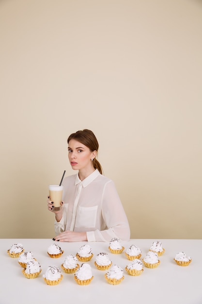 Serious young lady posing near cupcakes holding coffee