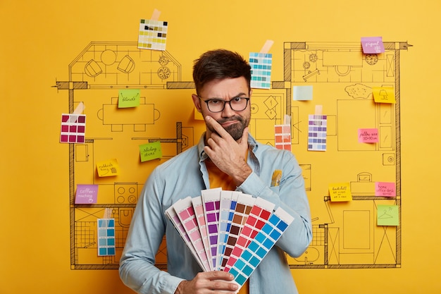 Serious young male stands next to house design sketch ready for
renovation