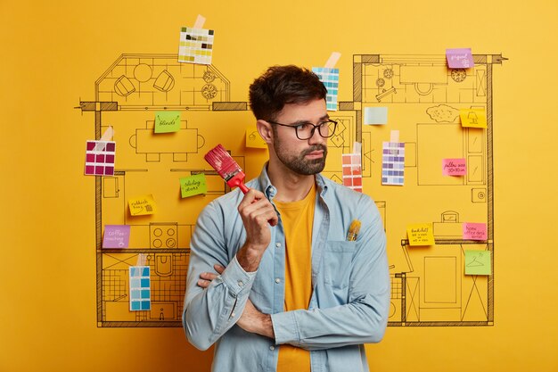 Serious young male stands next to house design sketch ready for renovation