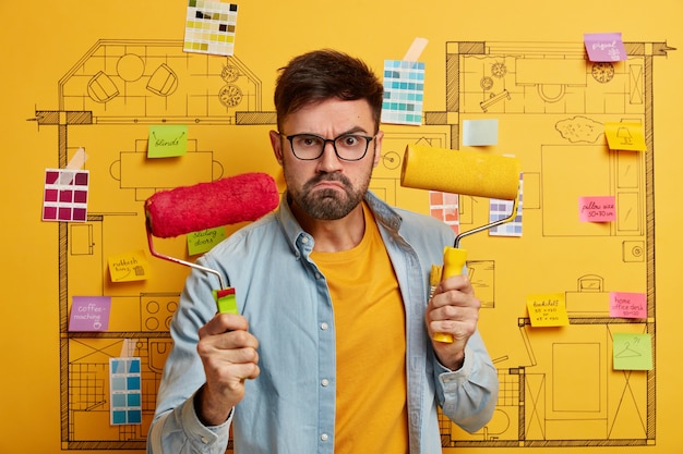 Serious young male stands next to house design sketch ready for renovation