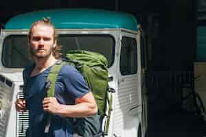 Free photo serious young man carrying backpack looking at camera at outdoors