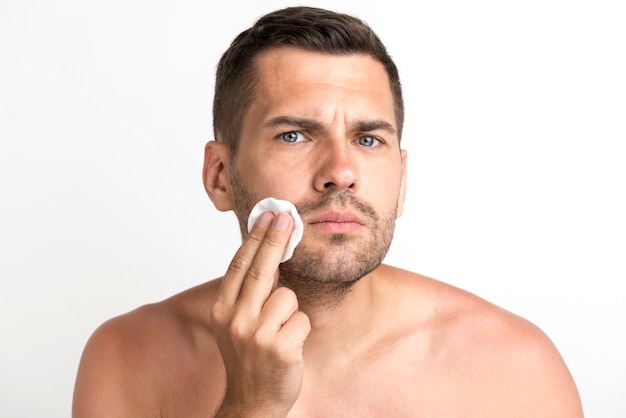 Serious young man cleaning his face against white background