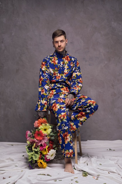 Free photo serious young man holding flower bouquet in hand looking at camera against grey wall