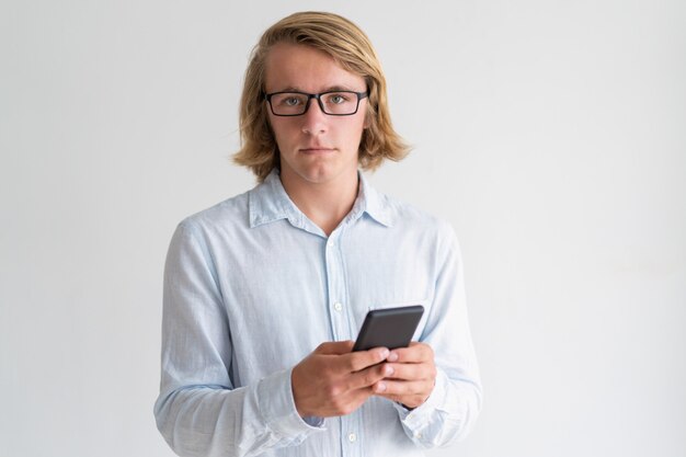 Serious young man holding and using smartphone