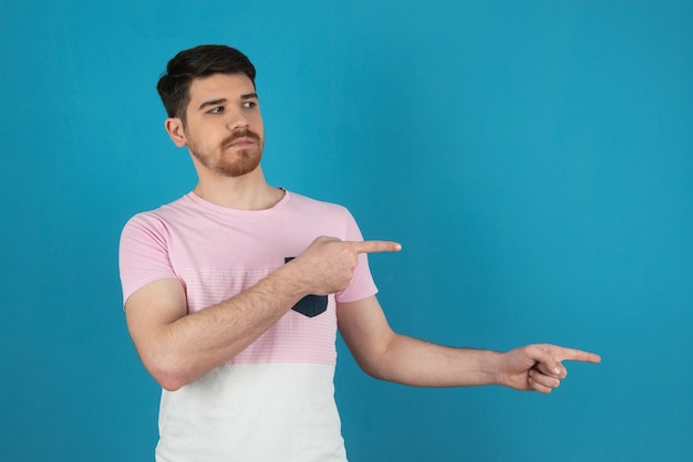 Serious young man pointing finger to the right side and looking away in a blue.