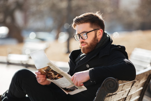 Free photo serious young man sitting and reading newspaper in the city